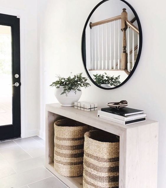 a modern entryway with an elegant wooden console, baskets for storage, a round mirror and a potted plant
