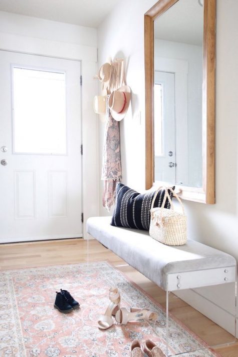 a modern, light-filled entryway with an acrylic-legged bench, a statement mirror, a boho rug and a clothes rack