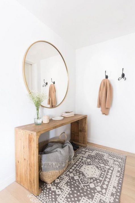 A modern, warm-colored entryway with a wooden bench, a round mirror, a printed rug and a basket with a blanket