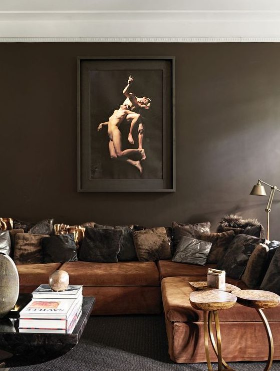 an atmospheric and exquisite living room with dark brown walls, a rust colored sofa and cushions, a coffee table and some lamps