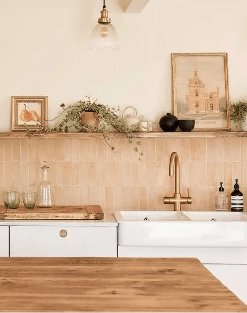 a neutral kitchen with white cabinets, a stacked pink zellige tile backsplash, open shelving and some decor