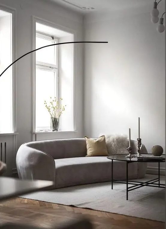 a neutral, minimalist living room with a curved sofa, a pendant lamp, a coffee table, pillows and flowers in a vase