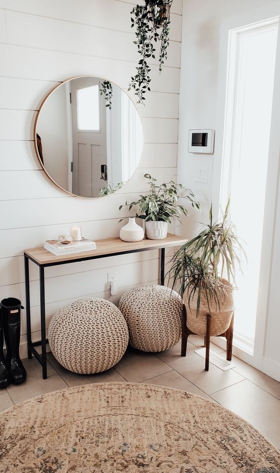 A neutral, modern entryway with a wooden console, crochet stools, potted plants and a round mirror is chic