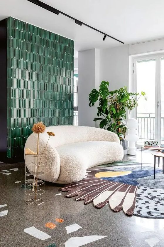 a whimsical living room with a green tile wall, a white curved bouclé sofa, a colorful rug, side tables and lots of greenery
