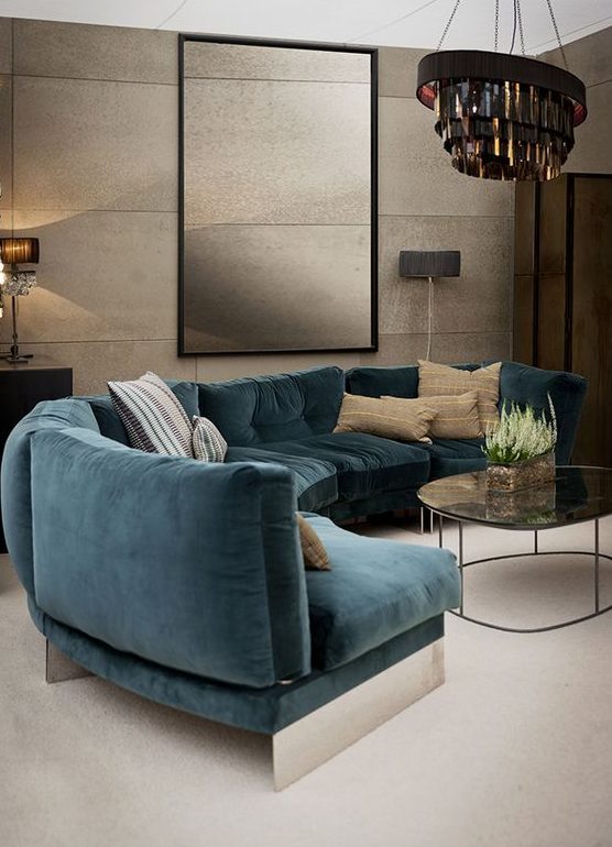an elegant living room with a curved turquoise sofa, a statement chandelier, light brown textured walls and chic lamps
