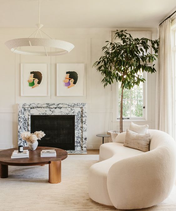 an elegant, neutral living room with crown molding, a white marble fireplace, a curved boucle sofa, a coffee table and some artwork
