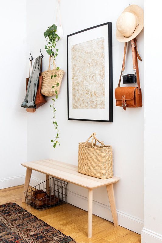 a simple, modern entryway with a wooden bench, a statement piece of art, a wire basket and hangers