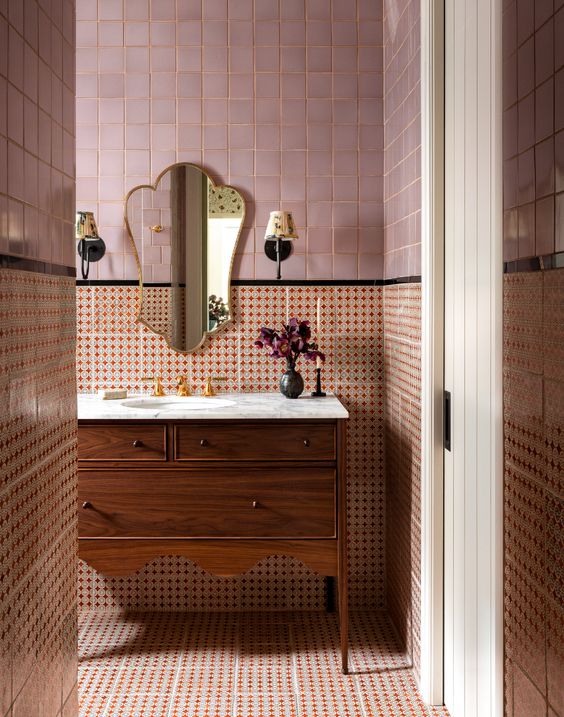 an elegant bathroom with pink zellige and red printed tiles, a stained scalloped vanity and a gorgeous mirror