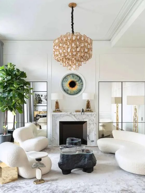 an elegant living room with a marble-clad fireplace, a curved cream sofa and matching chairs, black coffee tables and a whimsical chandelier