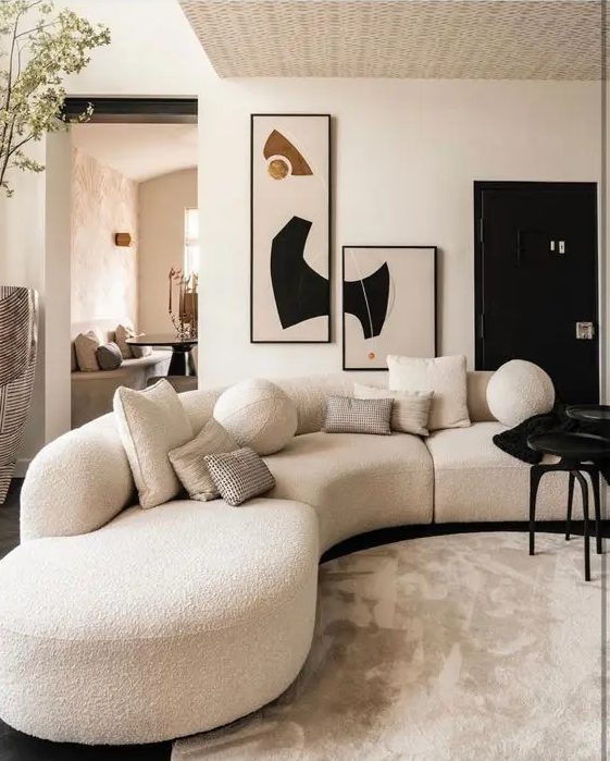 A stylish and contrasting living room with a white curved bouclé sofa, a black table and eye-catching artwork on the wall