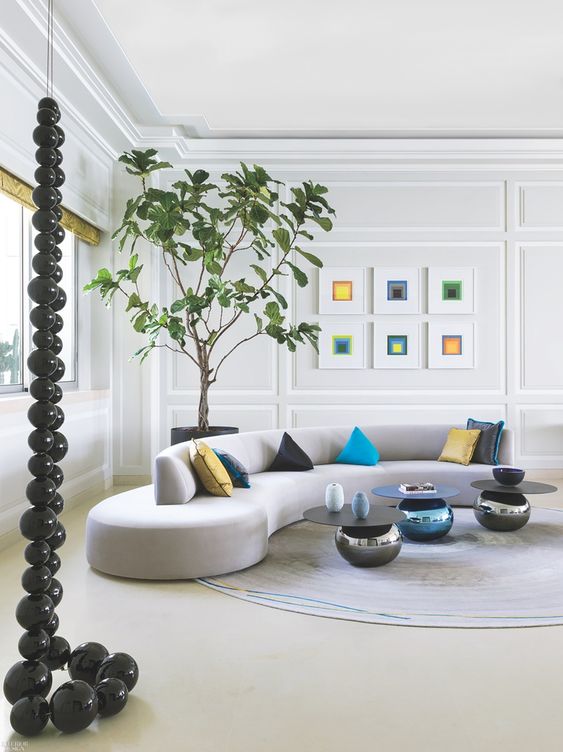 a stylish modern living room with crown molding, a gray curved sofa with colorful pillows, a gallery wall and coffee tables