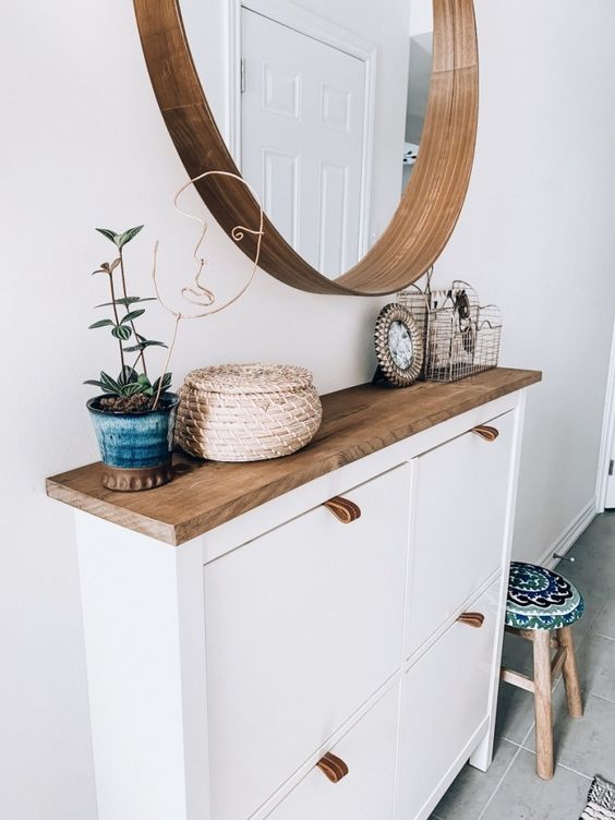 a stylish modern entryway with a chopped IKEA shoe cabinet, a round mirror and a potted plant