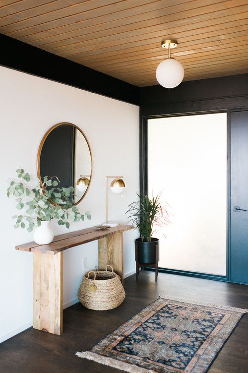 a stylish, modern entryway with a round mirror, a basket, a plant on a stand and a boho rug