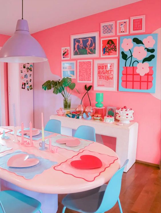 A dining room with super dopamine decor, pink walls, white tables and blue chairs, a purple pendant lamp, a bright gallery wall and eye-catching decor