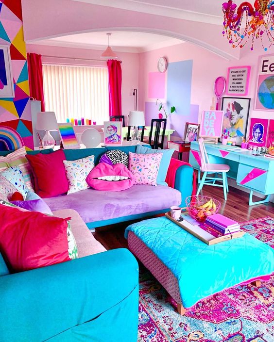 A super bright living room in dopamine decor with pink walls, a purple and turquoise sofa and ottoman, a statement rug, statement furnishings and a chandelier