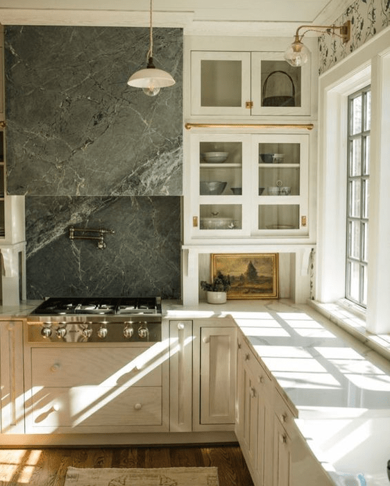 A vintage white kitchen with traditional and shaker cabinets, neutral countertops, a gray soapstone backsplash, and a range hood is a stylish idea