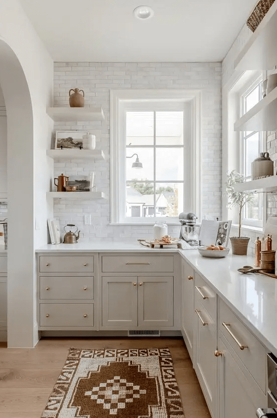 a white farmhouse kitchen with shaker cabinets, white stone countertops, a white marble tile backsplash, open shelving and some decor