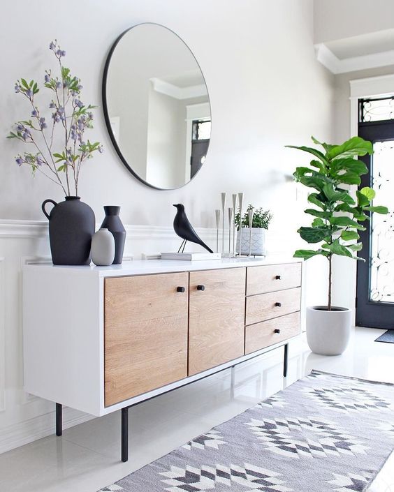 An airy, modern entryway with a mid-century sideboard, a round mirror, a statement plant and some decor