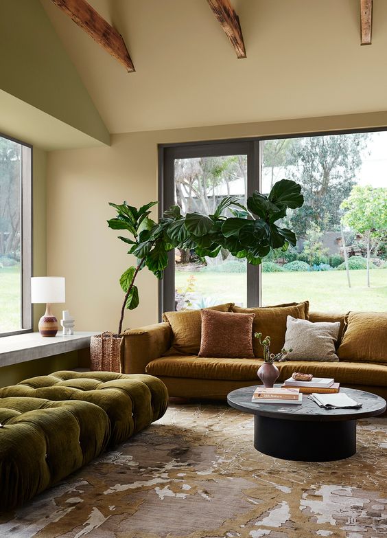 an earthy living room with a neutral and light green wall, a bold printed rug, a green tufted saybed and a mustard sofa