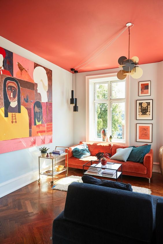 a particularly eye-catching living room with a red blanket, a red sofa, eye-catching art, a navy blue sofa and some pendant lamps