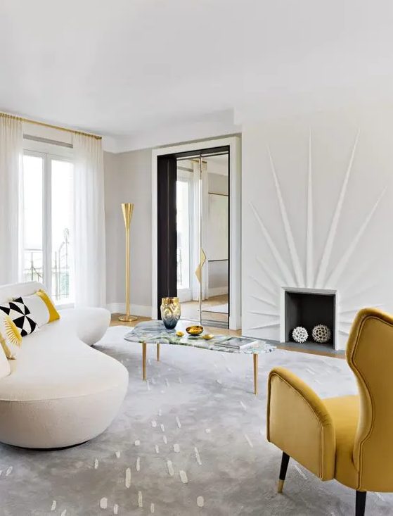 a striking living room with a fireplace, yellow wing chair, cream curved sofa, curved coffee table and gold accents