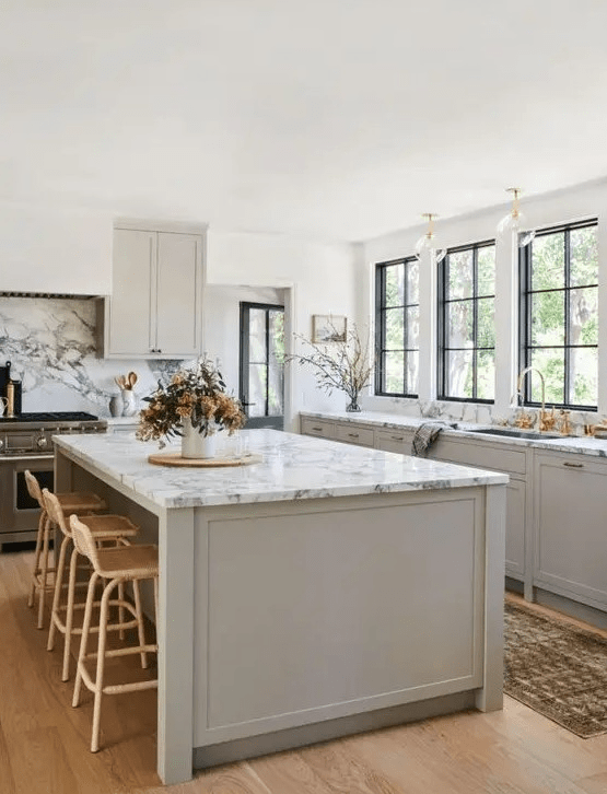 An inspiring dove gray modern farmhouse kitchen with shaker-style cabinets, white marble countertops, gold accents and rattan stools