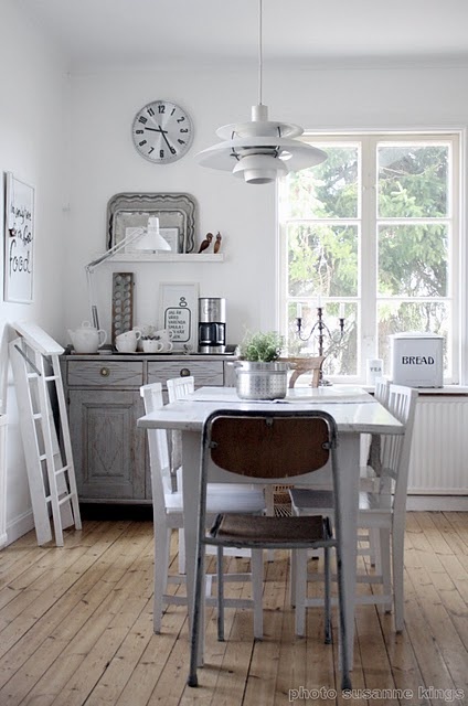 a neutral Scandinavian kitchen with white and gray shabby chic cabinets, a dining area accented by a hanging lamp and some decor