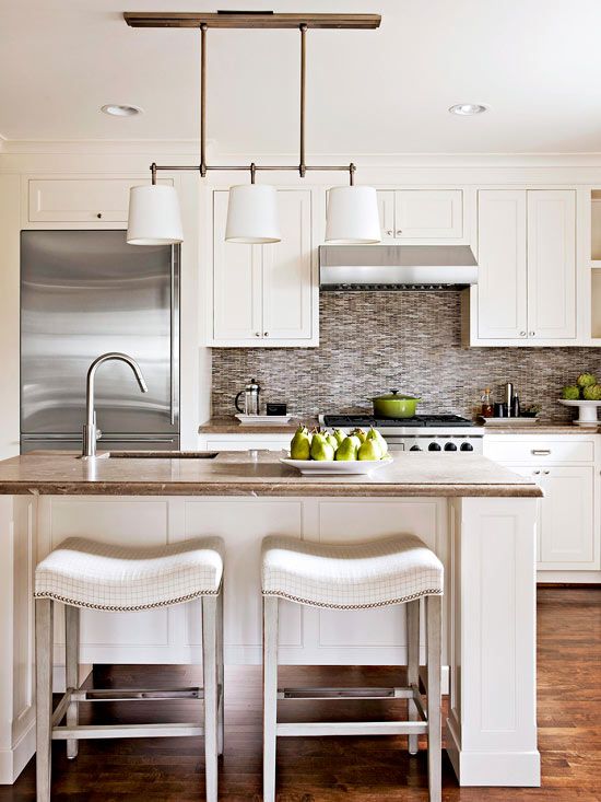 a modern white kitchen with shaker cabinets, stone countertops and tiled backsplash, pendant lamps and upholstered stools