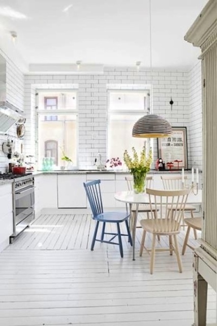 a white Scandinavian kitchen with just base cabinets, white subway tiles, a table and mismatched chairs, a pendant lamp and lots of light