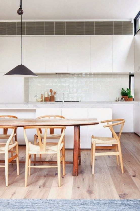 a stylish, modern white kitchen with sleek cabinets, stone countertops, a rustic table and chairs, and a pendant lamp