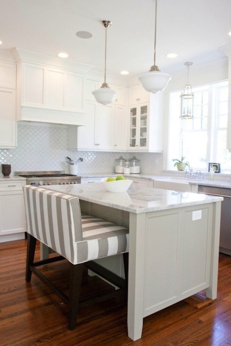 a modern, neutral kitchen with white cabinets and a gray island, a white tile backsplash and white countertops, a striped love seat and pendant lamps