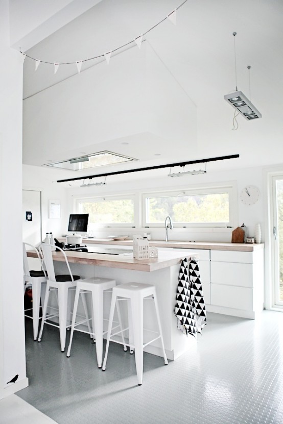 a white Scandinavian kitchen with elegant base cabinets, butcher block countertops, white stools and a window backsplash