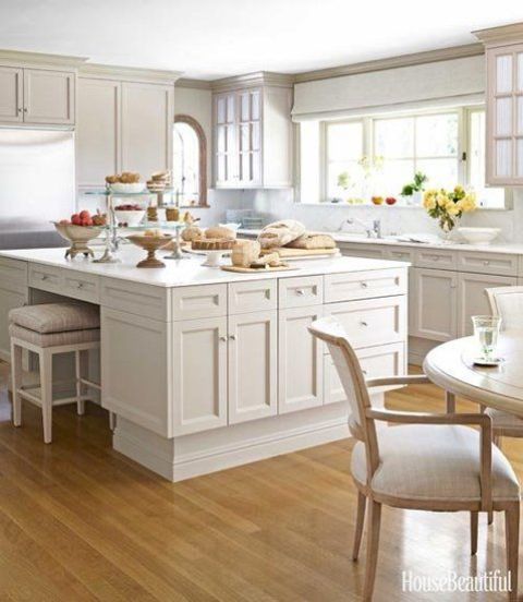 a tan cottage kitchen with shaker and glass cabinets, a large island, elegant chairs and a dining area