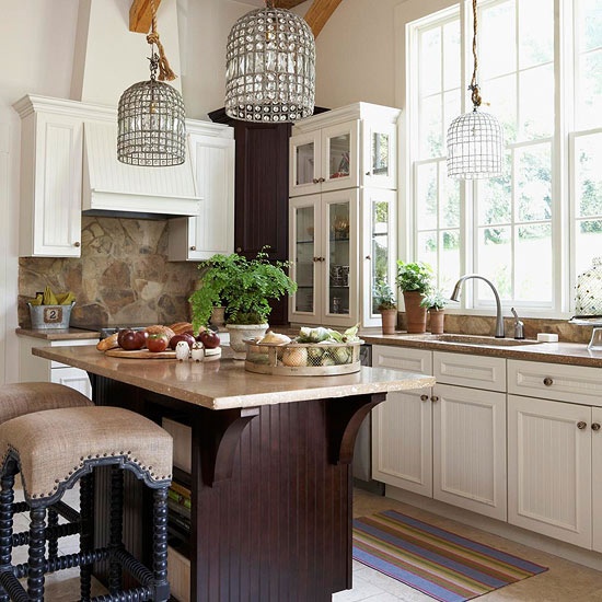 a neutral farmhouse kitchen with a deep purple kitchen island, stone countertops and backsplash, crystal pendant lamps and greenery
