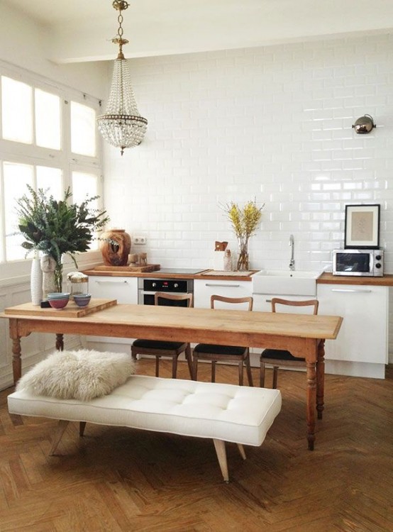 a white Scandinavian kitchen with butcher block countertops, a white subway tile wall, a vintage wooden table and matching chairs, and a statement chandelier