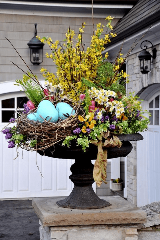 a bright outdoor Easter arrangement with yellow, purple, pink flowers, greenery and large blue artificial eggs