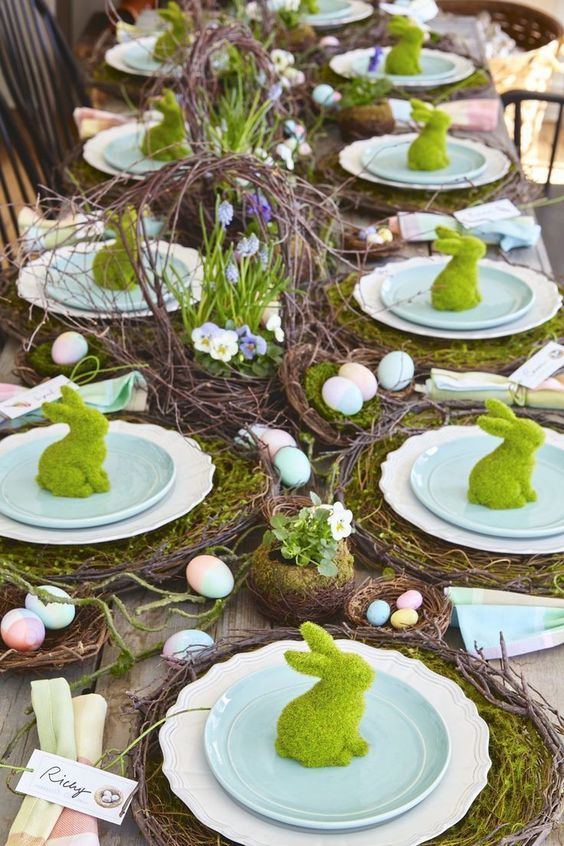 a bright, rustic Easter table with vine and moss placemats, artificial nests with colorful eggs and a vine centerpiece with flowers