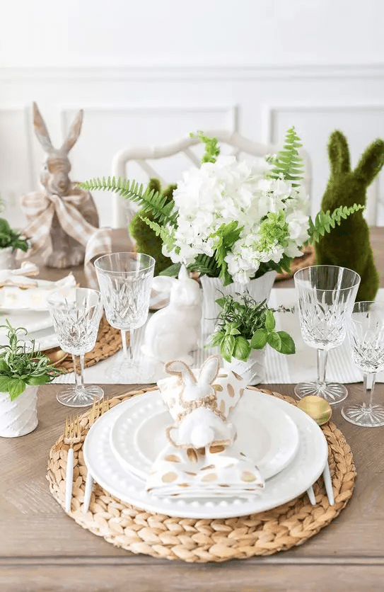 A charming Easter tablescape with a striped runner and polka dot napkins, woven placemats, greenery and white flowers, and trash cans