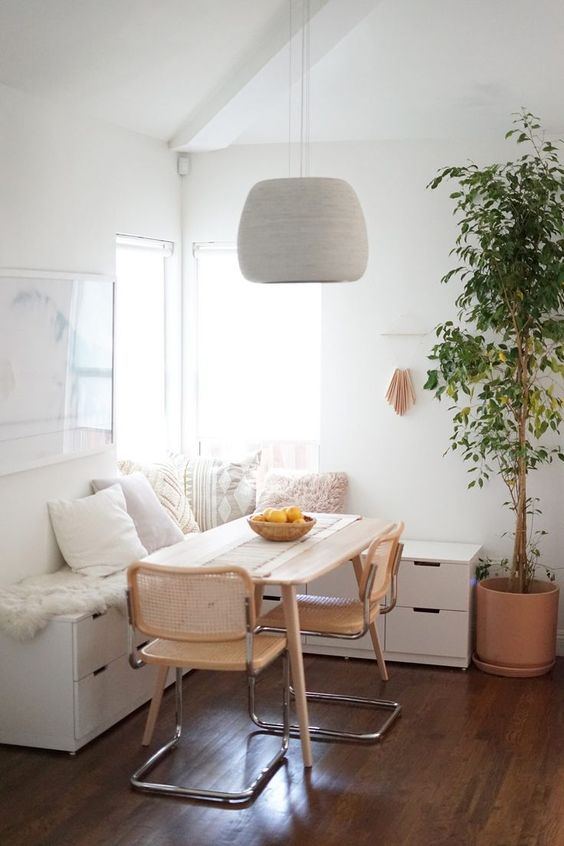 a cozy, modern breakfast nook with a white corner bench, a table and wicker chairs, a pendant lamp and some art