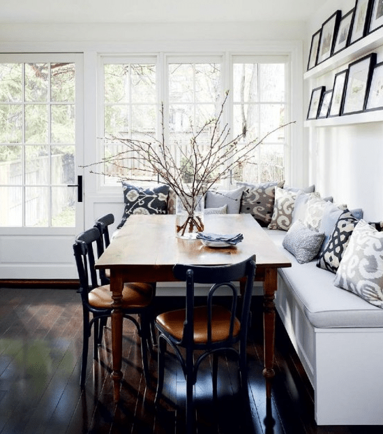 A farmhouse-style breakfast nook with corner benches, a stained table and black chairs, and a gallery wall