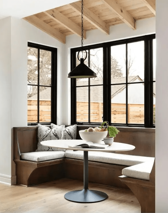 A fresh and natural dining area with a stained wood bench seat with neutral upholstery, an oval table and a black pendant lamp