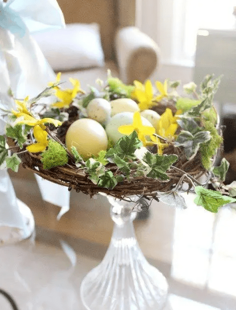 A glass stand with a nest, faux leaves, and speckled eggs is a chic and cool rustic Easter decoration you can make yourself
