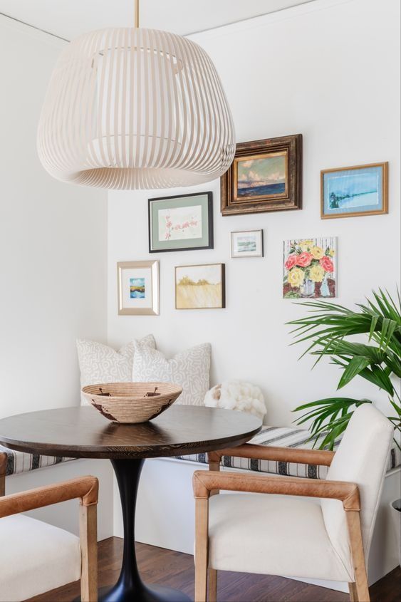 a vibrant breakfast nook with a corner bench, a stained table and cream chairs, a pendant lamp and a bright gallery wall