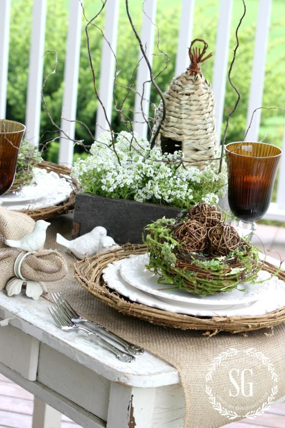 A beautiful rustic Easter tablescape with burlap napkins and runners, woven placemats, nests with greenery, flowers and branches is beautiful