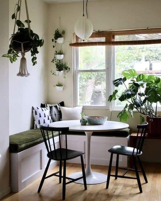 A modern boho style breakfast nook with a seating area, white table, black chairs, potted plants and some lighting