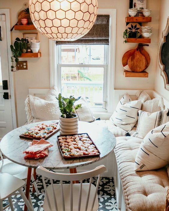 A modern farmhouse meets boho breakfast nook with a corner bench with pillows, a table and chairs, a hanging lamp, and dishes and decor on the shelves