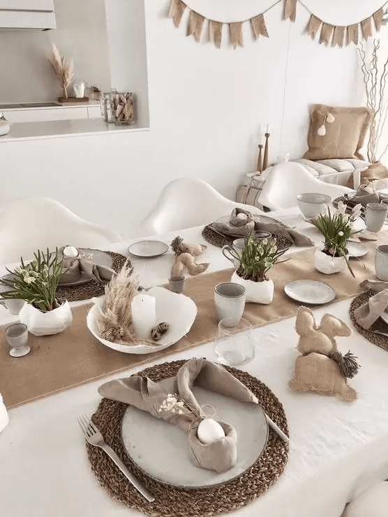 a neutral Easter tablescape with a burlap runner, woven table decorations, neutral linens, burlap bunkers, potted flowers and candles
