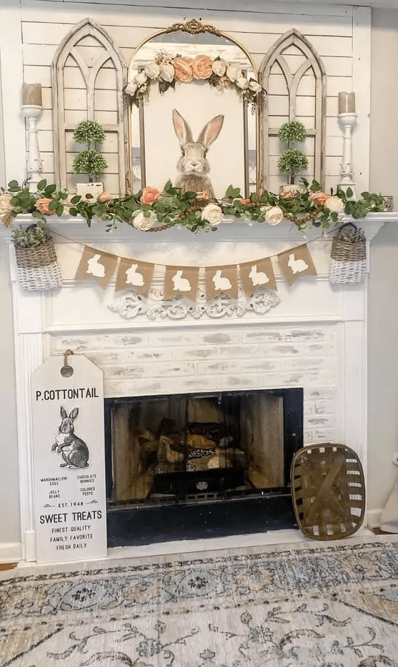 a pretty, rustic Easter mantel with a burlap banner, baskets, greenery and artificial flower garlands, a bunny artwork, some green topiaries and candles