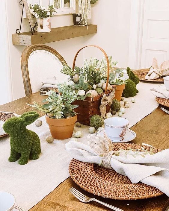 A pretty rustic Easter table setting with a wooden basket with eggs, flowers and moss, artificial eggs, moss bunnies and woven placemats is cool