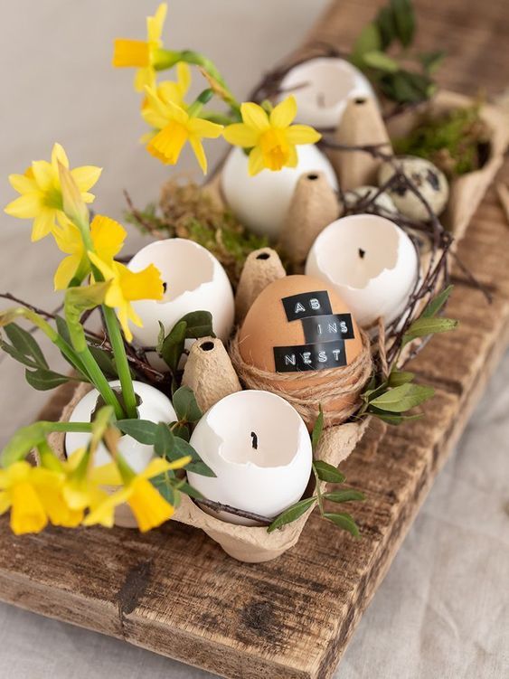 A rustic Easter centerpiece made from an egg carton with eggshell candles and bright yellow flowers is a cool solution